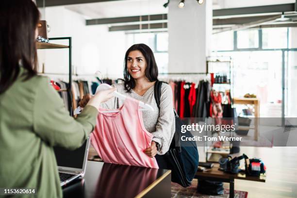 woman handing dress to clothing store cashier - buying clothes stock-fotos und bilder