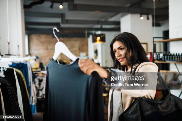 woman looking at blouse while out shopping - loja de roupas - fotografias e filmes do acervo
