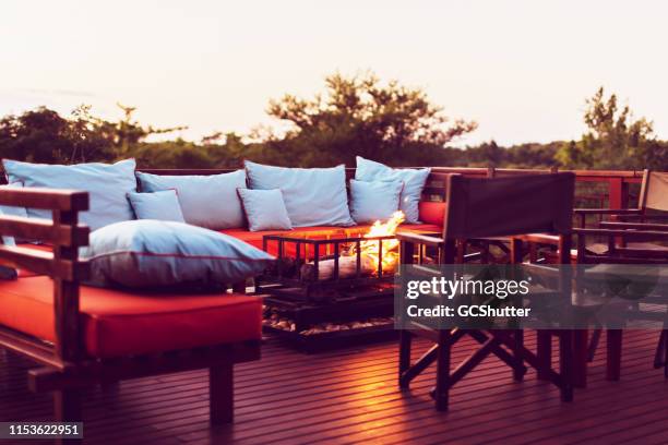 romantic setting on a wooden deck with fireplace and outdoor furniture at a holiday resort in africa - safari lodge stock pictures, royalty-free photos & images