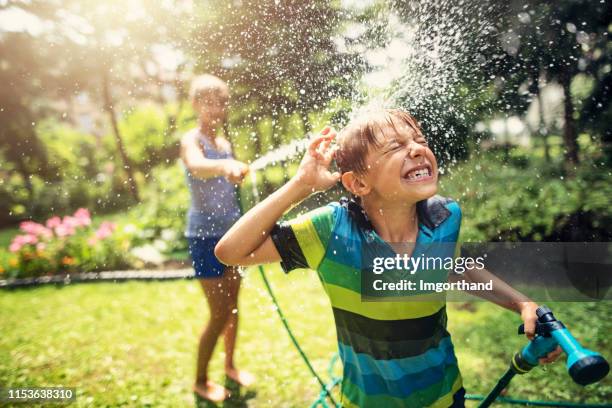 children having garden hose fun in back yard - hosepipe stock pictures, royalty-free photos & images