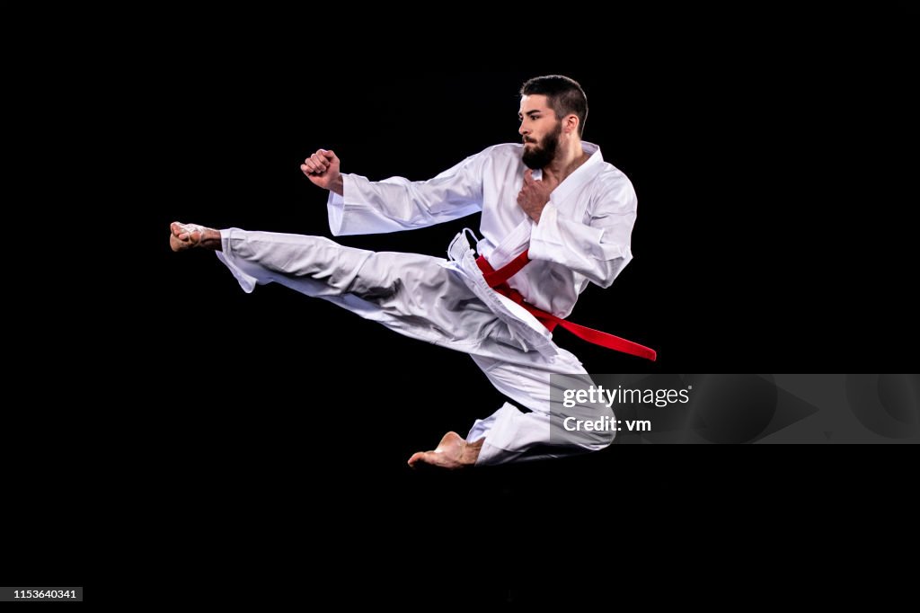 Hombre en kimono realizando una patada voladora contra un fondo negro