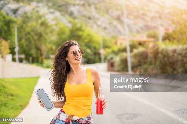 happy young woman listening to music and drinking juice in the neighborhood. - music speaker stock pictures, royalty-free photos & images
