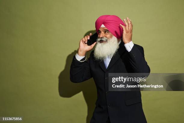 a senior sikh man wearing a pink turban or dastar and a smart suit speaking on a mobile phone - sijismo fotografías e imágenes de stock