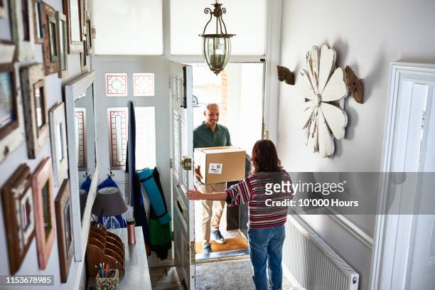 delivery man giving parcel to woman in hallway - receiving box stock pictures, royalty-free photos & images