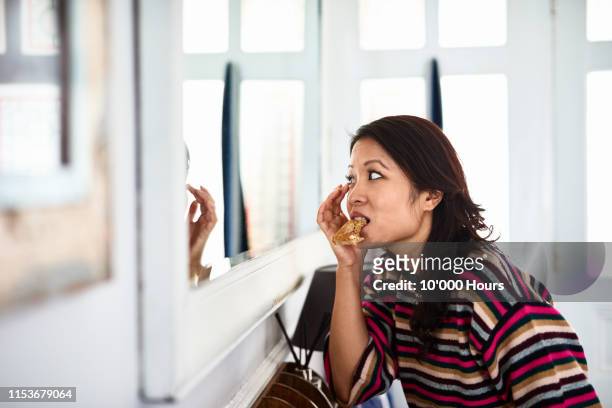 mid adult woman checking herself in hall mirror and eating toast - dringendheid stockfoto's en -beelden