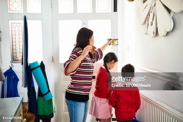 Mother eating toast and opening front door for two school children