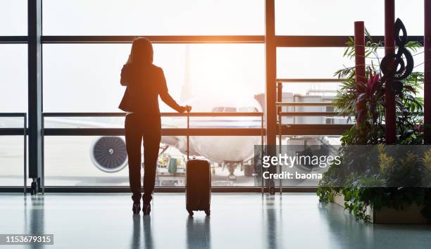 silhouette of business traveler makes a call while waiting for her flight - business travel asian stock pictures, royalty-free photos & images
