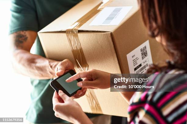 woman using smartphone to sign for parcel delivery - repartidor fotografías e imágenes de stock