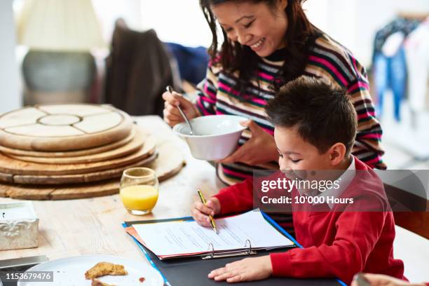 cheerful boy in school uniform doing homework with mother smiling - filipino family eating stock pictures, royalty-free photos & images