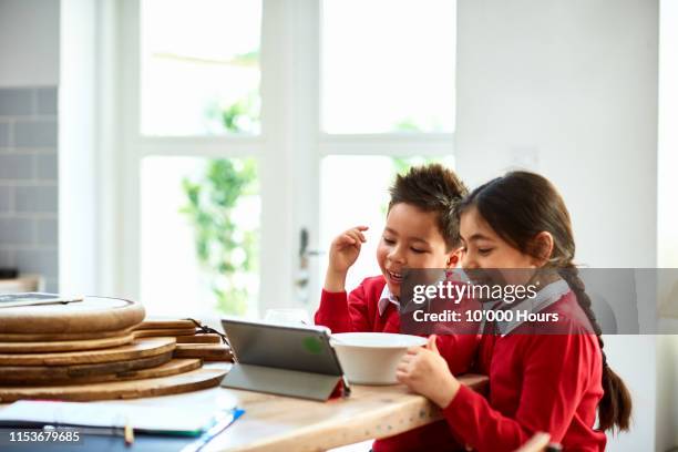 Brother and sister watching tablet at breakfast and smiling