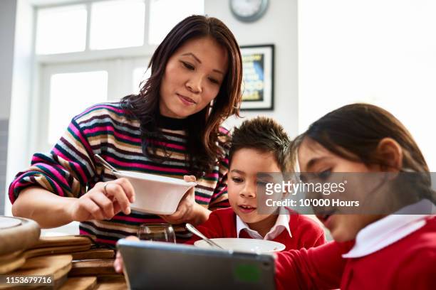 woman in her 30s eating cereal and showing two children digital tablet - daily life in philippines stock pictures, royalty-free photos & images