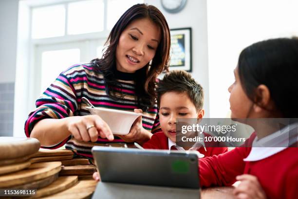 mother eating cereal looking at tablet with two children - vietnamesischer abstammung stock-fotos und bilder