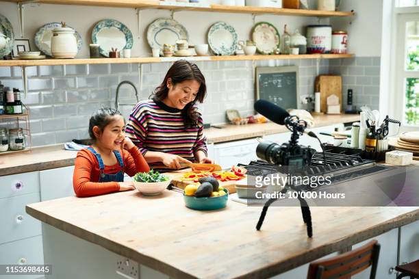 woman chopping food in kitchen with daughter - cooking show stock-fotos und bilder