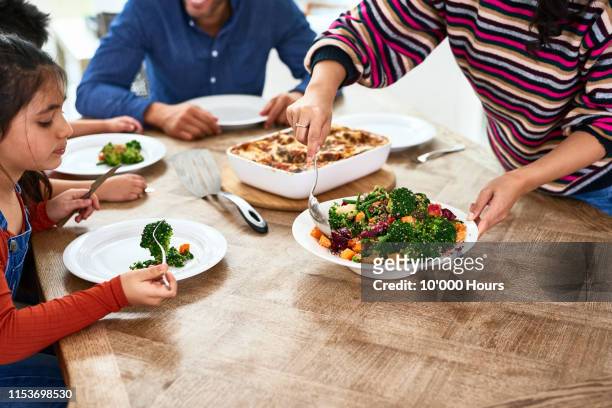 cropped view of woman serving vegetables to family - parenting dinner kids stock-fotos und bilder