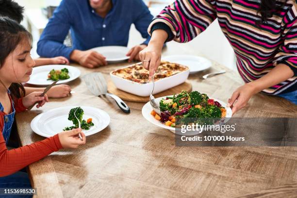 cropped view of woman serving vegetables to family - mesa de jantar - fotografias e filmes do acervo