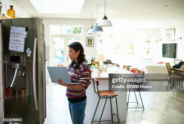 woman using laptop by fridge and buying food online - shopping list stock pictures, royalty-free photos & images
