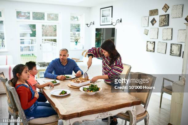 mid adult woman serving family dinner to husband and children - dining table stock pictures, royalty-free photos & images
