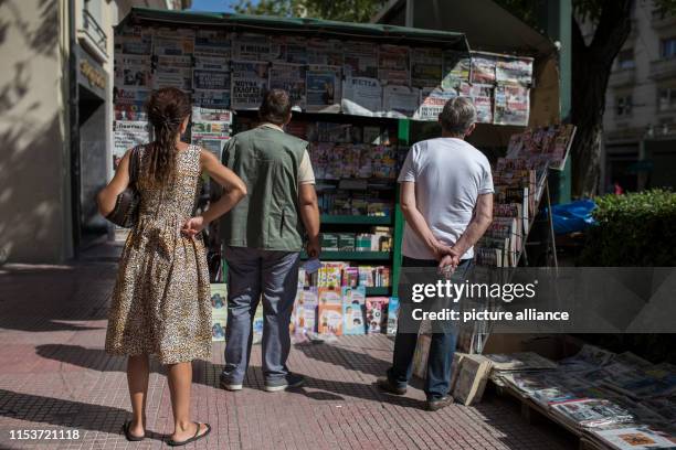 July 2019, Greece, Athen: Passers-by read the front pages of the newspapers at a kiosk. On Sunday the Greek voters are likely to reject extreme...