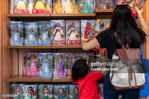 Visitors look through a shelf of doll for sale at Walt Disney Co.'s Shanghai Disneyland theme park towards the iconic castle during a trial run ahead...