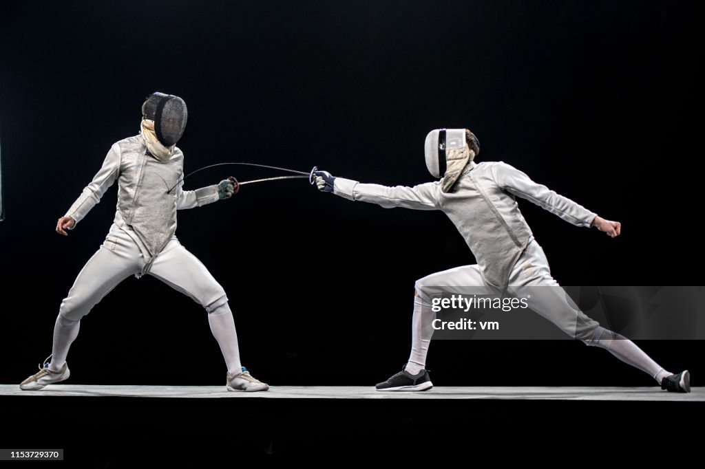 Two fencers fighting in front of a black background