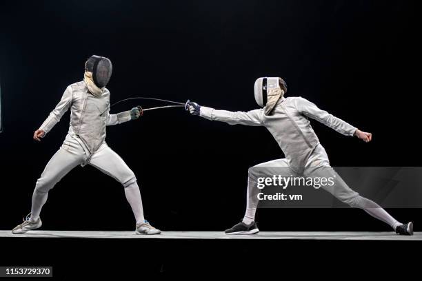 two fencers fighting in front of a black background - fechten stock pictures, royalty-free photos & images