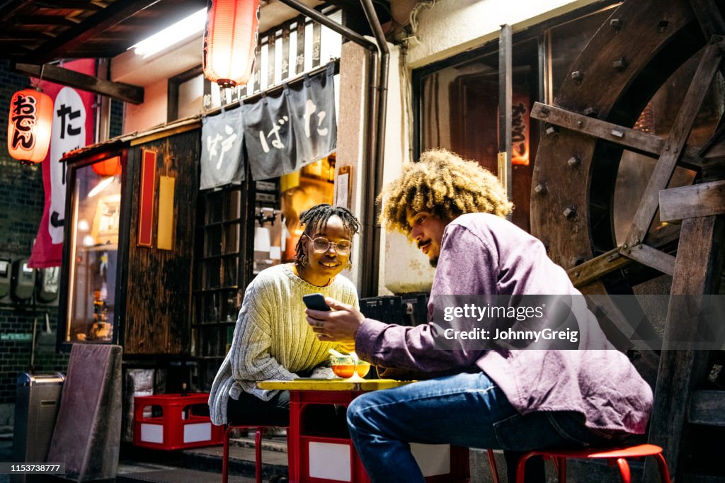 Hipster couple looking at smartphone outside restaurant