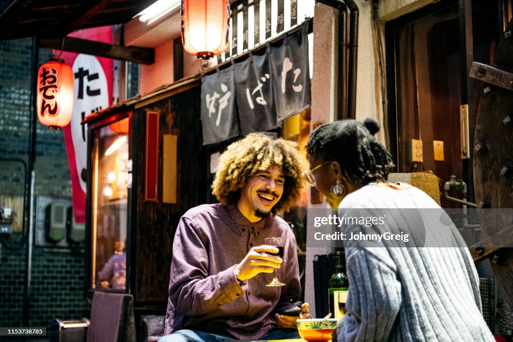 Attraktives Paar lacht mit Wein vor dem japanischen Restaurant