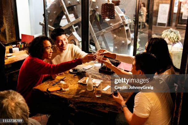 candid portrait of four friends toasting drinks at restaurant table - izakaya stock pictures, royalty-free photos & images