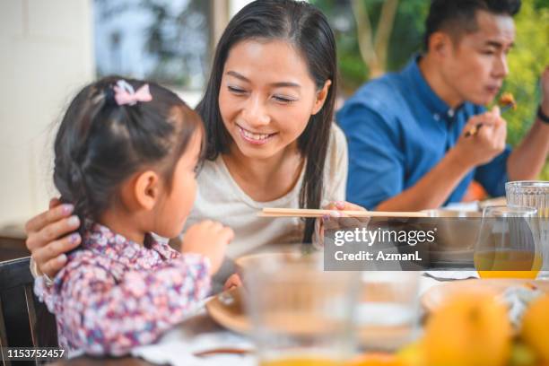 smiling woman looking at girl eating in back yard - chinese eating backyard stock pictures, royalty-free photos & images