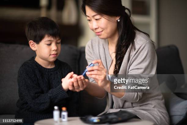 mother helping son check blood sugar levels - child diabetes stock pictures, royalty-free photos & images