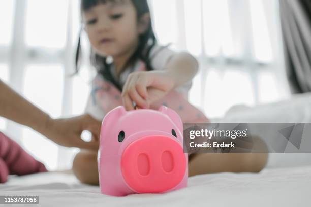 cute piggy bank with baby girl puts coins inside beside mother - save our future babies stock pictures, royalty-free photos & images