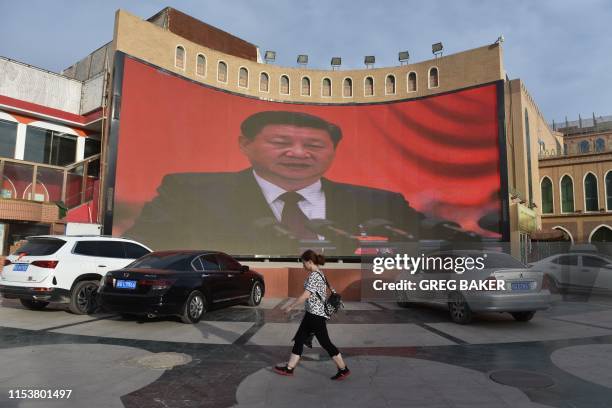 This photo taken on June 4, 2019 shows people walking past a screen showing images of Chinese President Xi Jinping in Kashgar, in China's western...