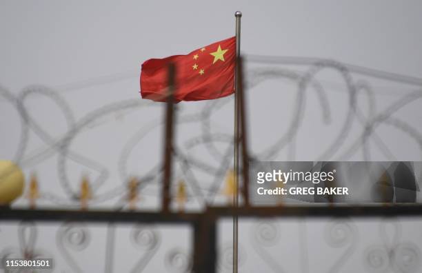 This photo taken on June 4, 2019 shows the Chinese flag behind razor wire at a housing compound in Yangisar, south of Kashgar, in China's western...