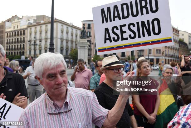 Man holds a placard saying, 'Maduro Asesino' during the protest. Around a hundred Venezuelans nationals gathered at Isabel II Square in Madrid to...