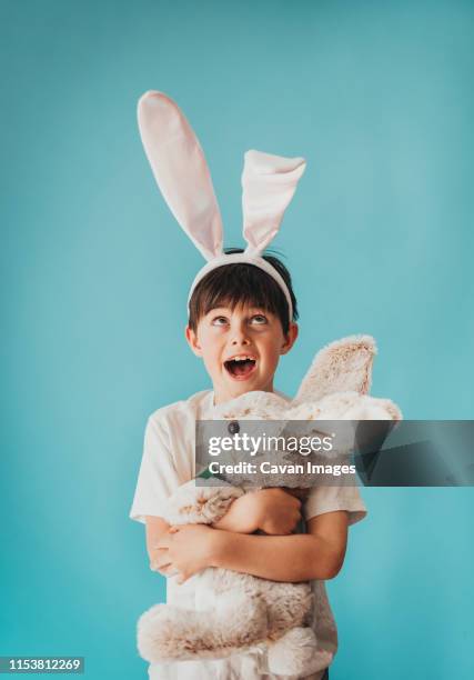 boy holding stuffed rabbit looking up at bunny ears on his head. - bunny ears stockfoto's en -beelden