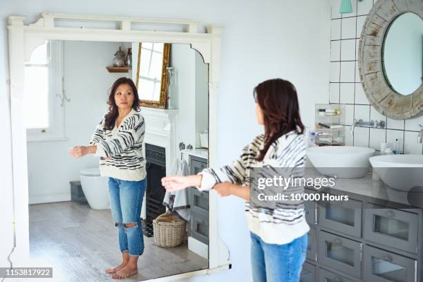 mid adult woman getting dressed and looking in mirror - preocupación por el cuerpo fotografías e imágenes de stock
