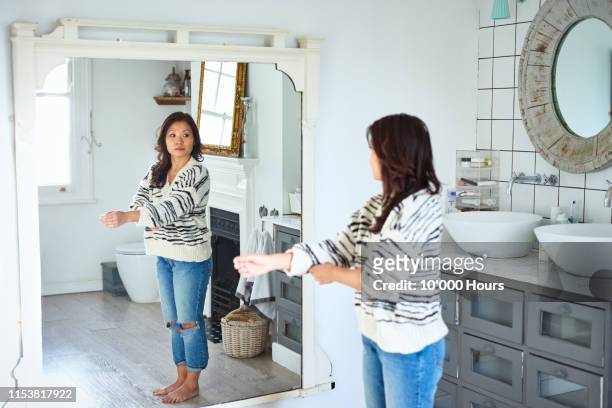 mid adult woman getting dressed and looking in mirror - 体への関心 ストックフォトと画像