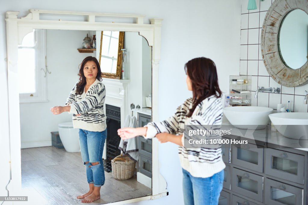 Mid adult woman getting dressed and looking in mirror