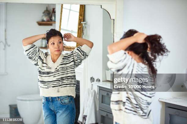 mid adult woman putting hair up and looking in mirror - survivor 10 stock pictures, royalty-free photos & images