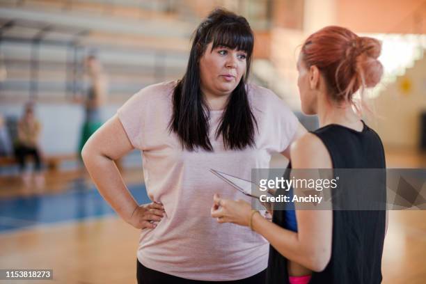 Fitness instructor with digital tablet talking with woman in gym