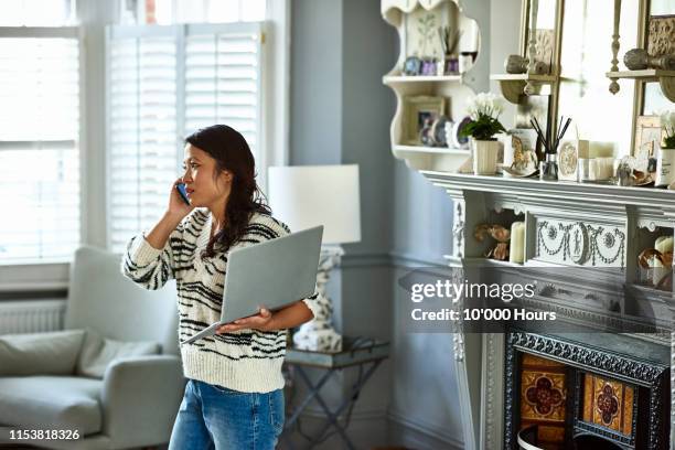 woman holding laptop and listening on smartphone - complaining foto e immagini stock