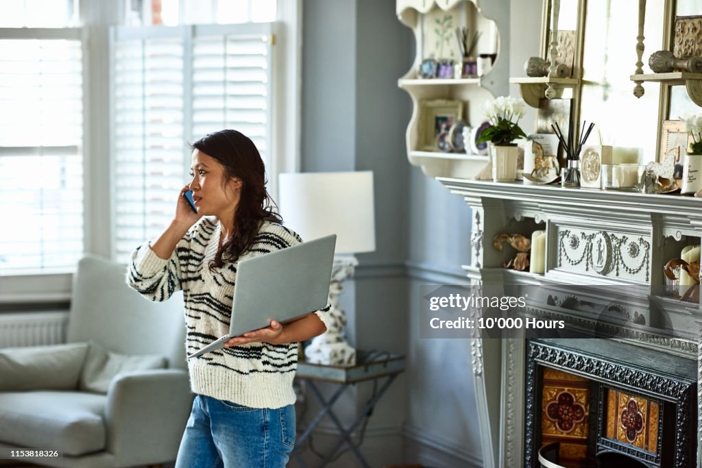 Woman holding laptop and listening on smartphone