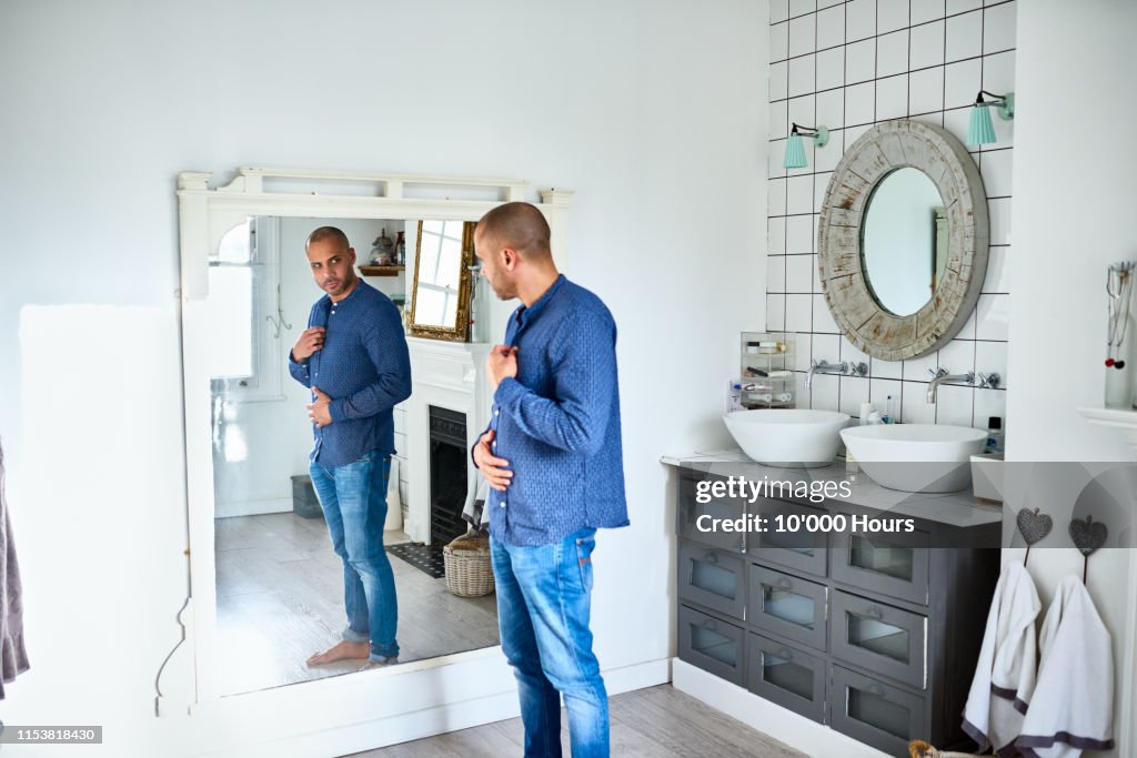 Mature man checking himself in bathroom mirror and touching tummy