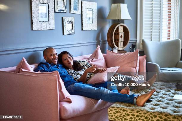 couple at home watching television together on sofa - asian man barefoot foto e immagini stock