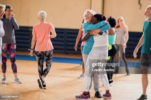 dame aînée soutenant la jeune femme sur leur classe de zumba - club de remise en forme photos et images de collection