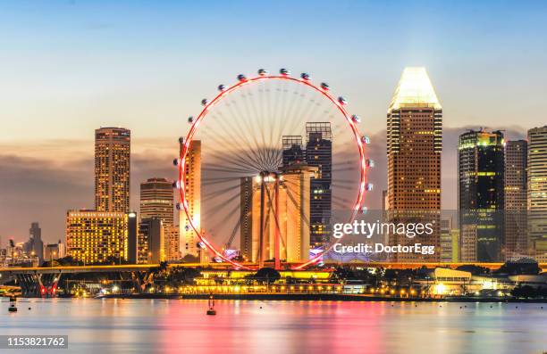 illumination of singapore fly giant ferris wheel with skyscraper buildings background at marina bay, singapore - singapore flyer stockfoto's en -beelden