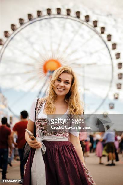 young blond woman standing in front of feriss wheel - oktoberfest fotografías e imágenes de stock
