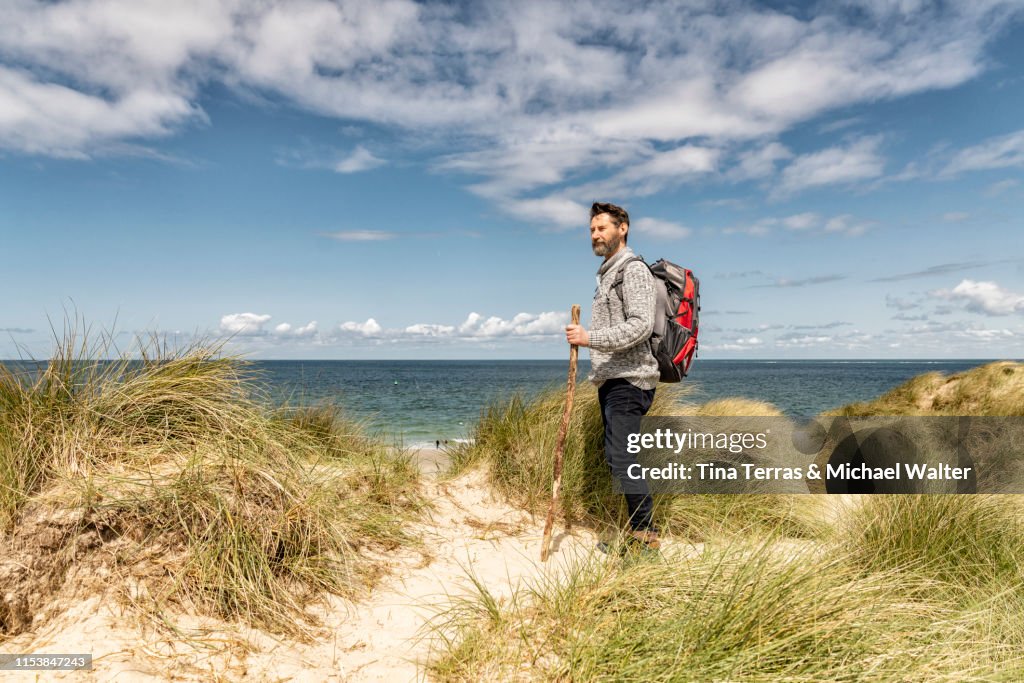 Man hiking in sand dunes on the beach.