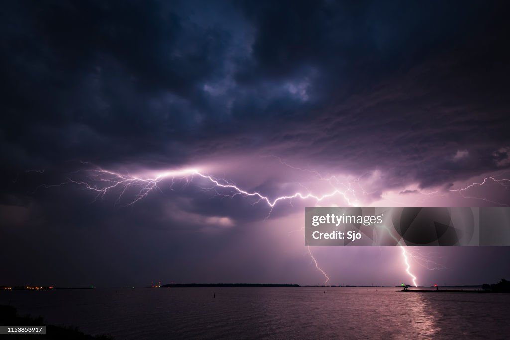 Lightning in the dark night sky over a lake during summer