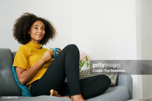 woman relaxing on sofa with hot drink - yellow sofa stock pictures, royalty-free photos & images